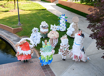 Several students gather together wearing colorful paper mache costumes with ribbons and other craft materials.